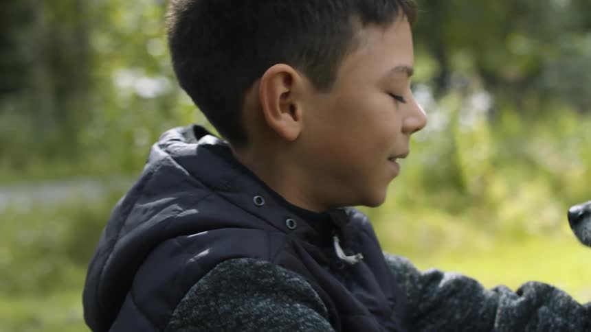 A boy sitting and playing with a dog with plants in the background