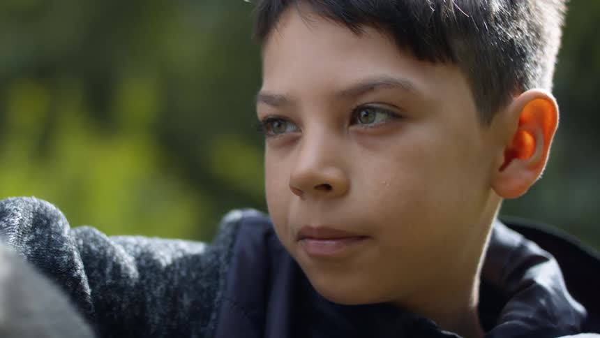 A boy sitting with plants in the background