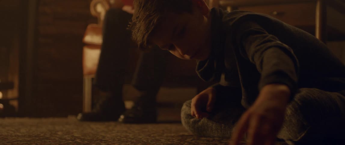 Man sits in chair reading while boy plays with toy car