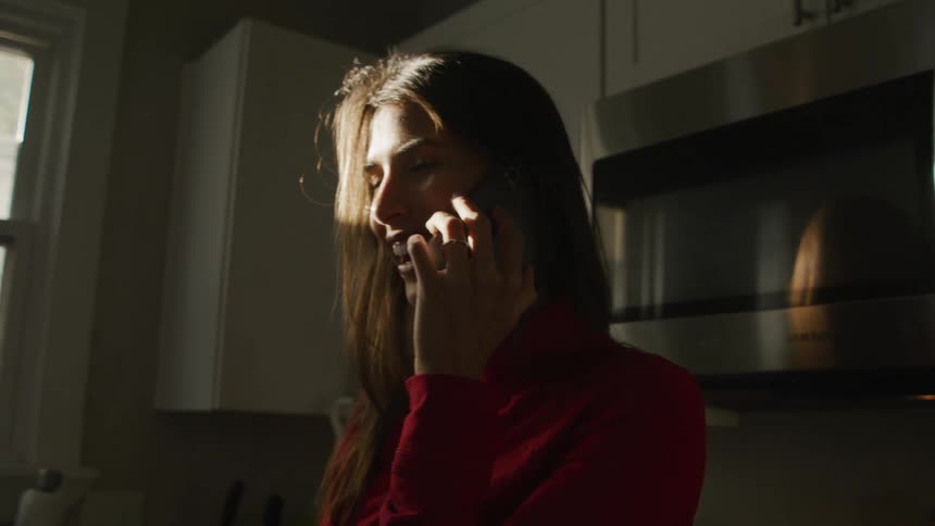 A young woman smiling while talking on the phone in a kitchen