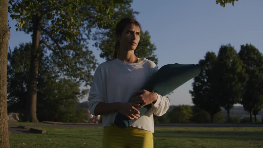 A woman is walking through a park carrying a bundle and looks upset