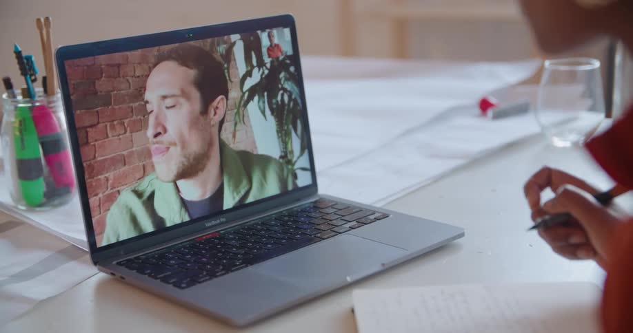 A woman is sitting at a table having a video call with a man on her computer