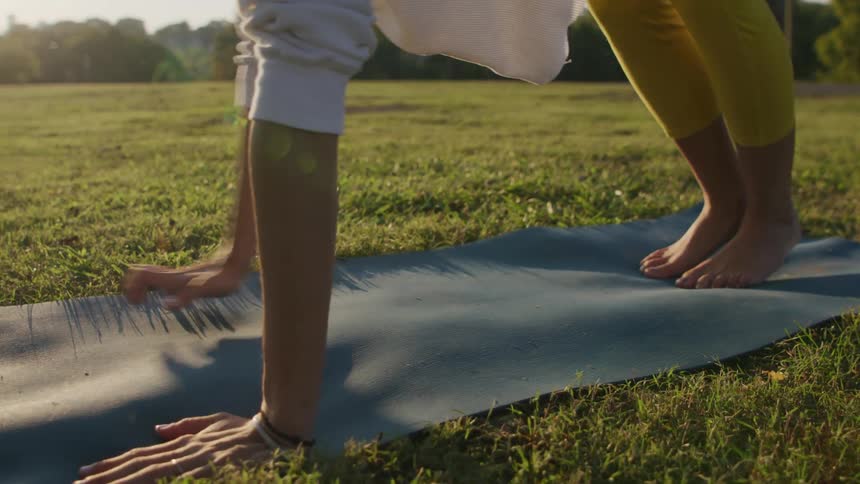 A woman practices yoga on a mat on a grassy field