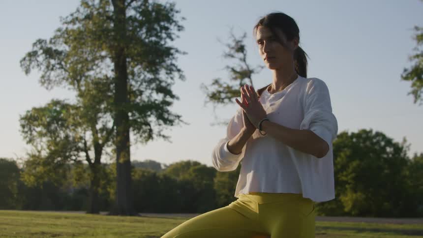 A woman stretches and holds a yoga pose standing on one leg in the grass