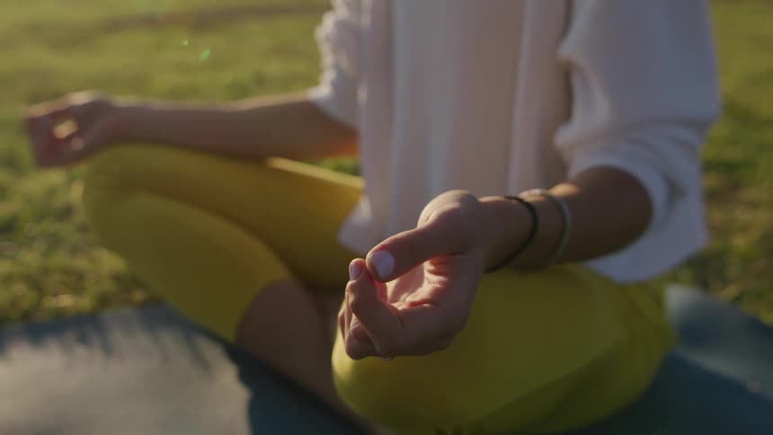 A woman sitting on an exercise mat with trees the sky and clouds in the background