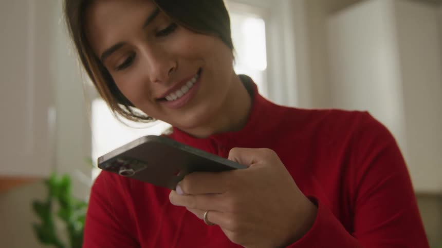 A woman smiles while looking at the screen of her smartphone