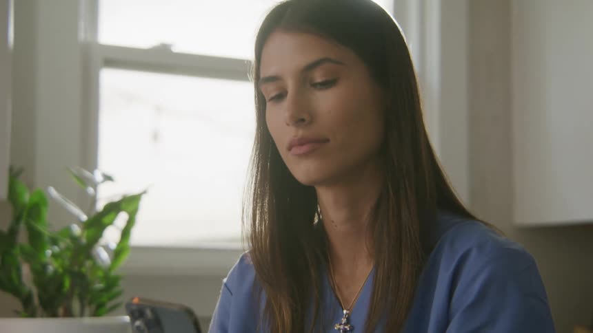 A woman in medical scrubs stops using her laptop to answer the phone