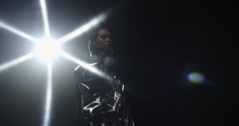 Woman poses in silver outfit that reflects bright glaring spotlight in dark area