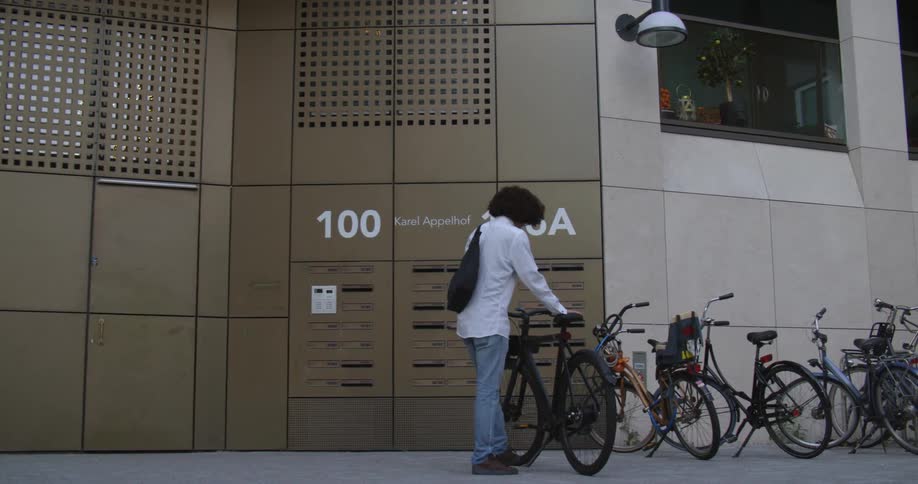 A man with a bag and glasses taking a bicycle from in front of a building