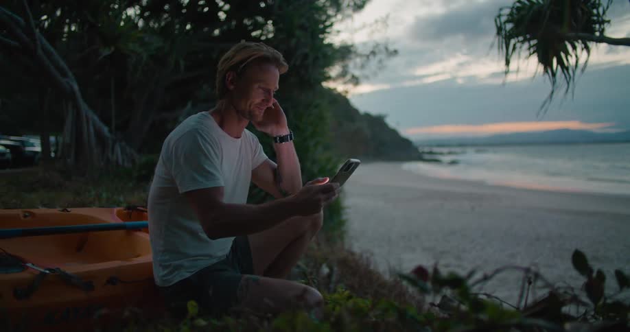 A man sitting at the beach looking at a smartphone