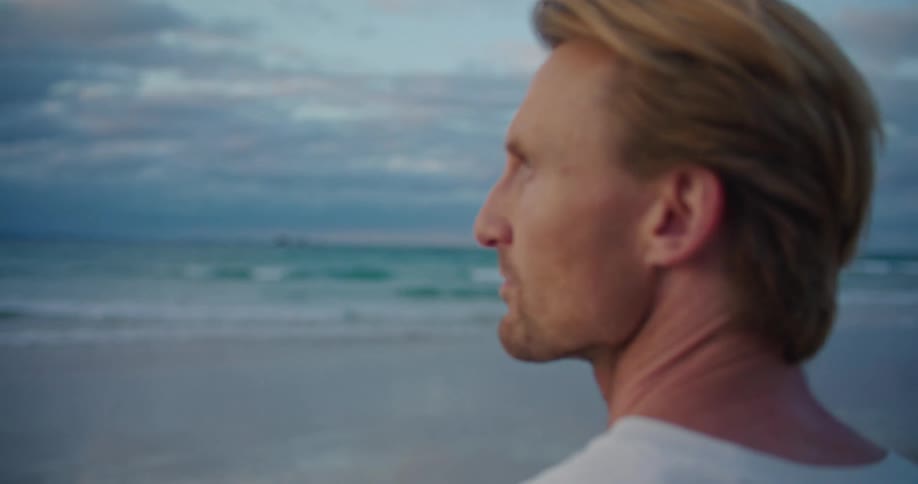 A man stands on the beach watching the waves roll in and then turns to look to the left of him