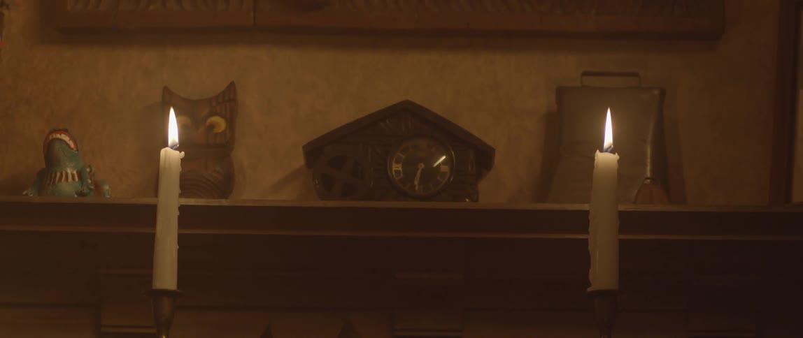 A clock and other items on a mantle behind two burning candles