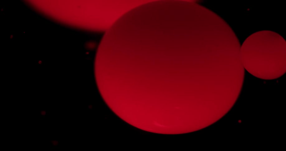 Big red ink bubbles floating on liquid in front of black background