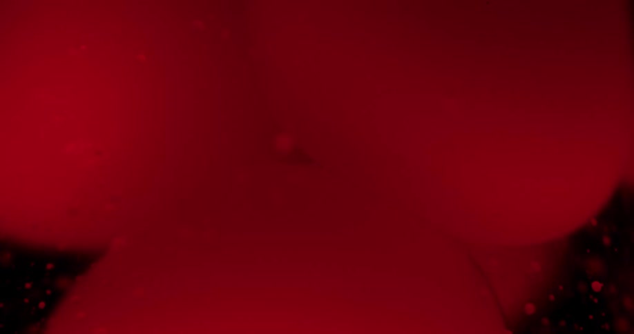 Red dark ink bubbles floating on liquid in front of black background