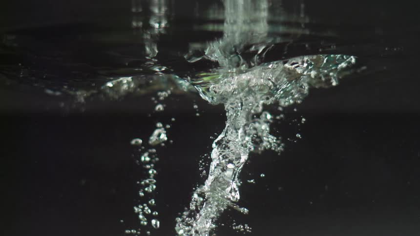 Green fruit plunges into water leaving bubbles and collapsing vortex
