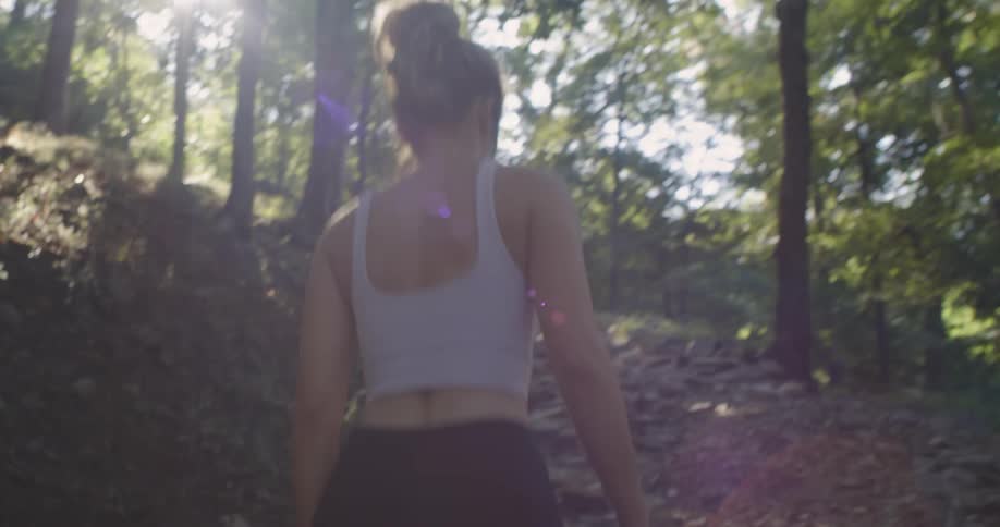 A woman walks a sloped trail through the trees on a bright sunny day