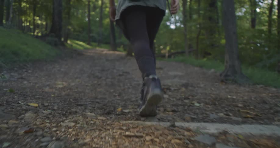 Woman with black pants and hiking shoes walks along a forest track