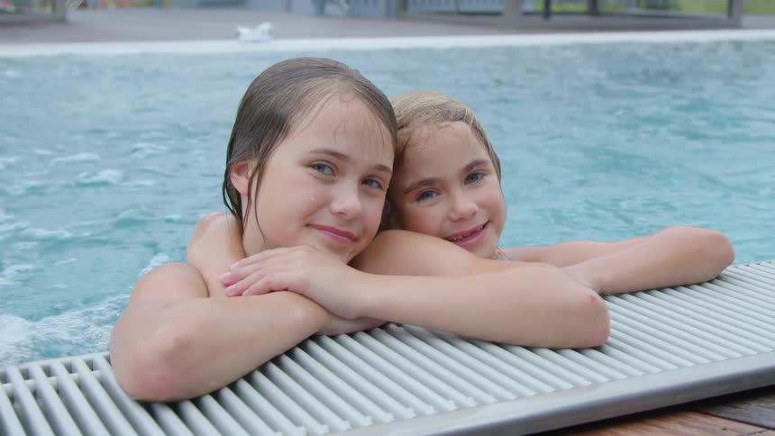 Two young girls pose together while in a swimming pool