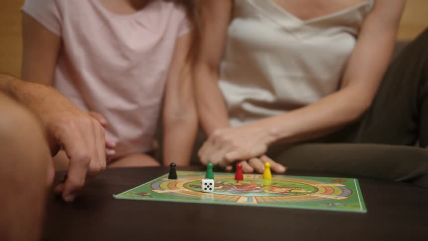 A girl roles dice while playing a board game with family