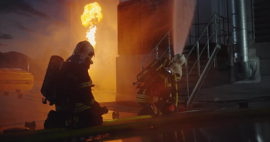 A firefighter stands behind a building as a nearby home burns in a fire