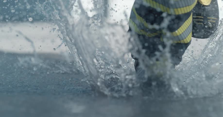 Puddle water splashes up as firefighter boots run through