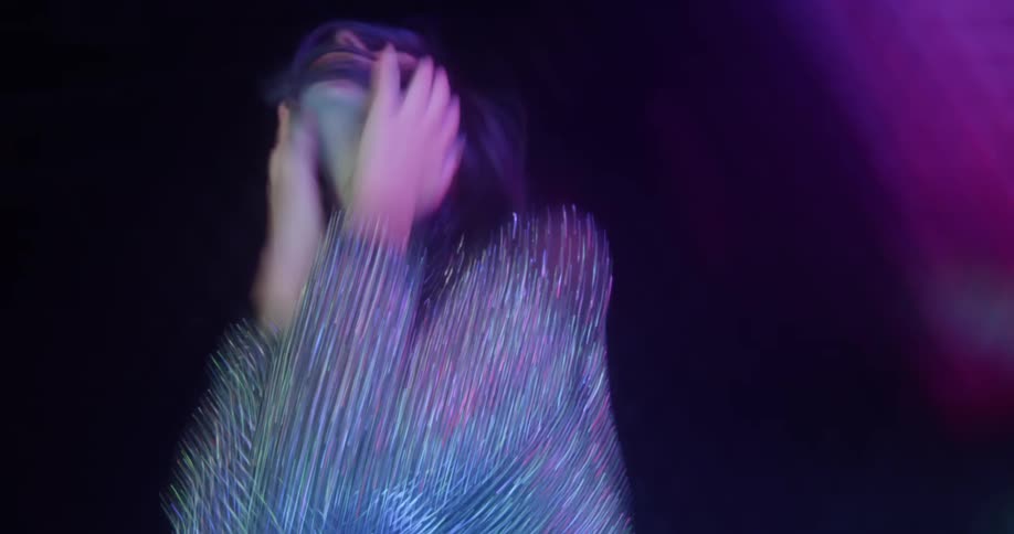 Woman wearing reflective outfit moves and poses on dark stage