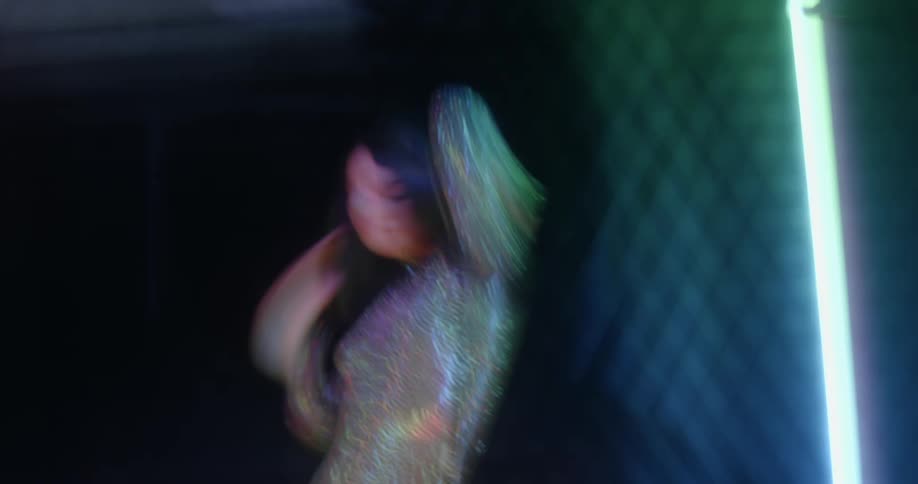 A woman wearing a sparkly costume dances and blurs as colorful lights glow