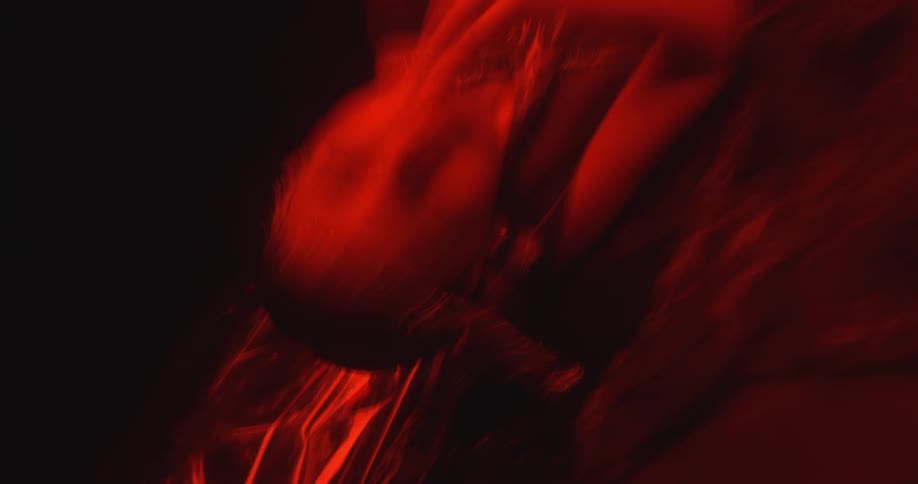 In a dark room with red lighting a woman laying on the floor begins to get up while the camera films in stop motion