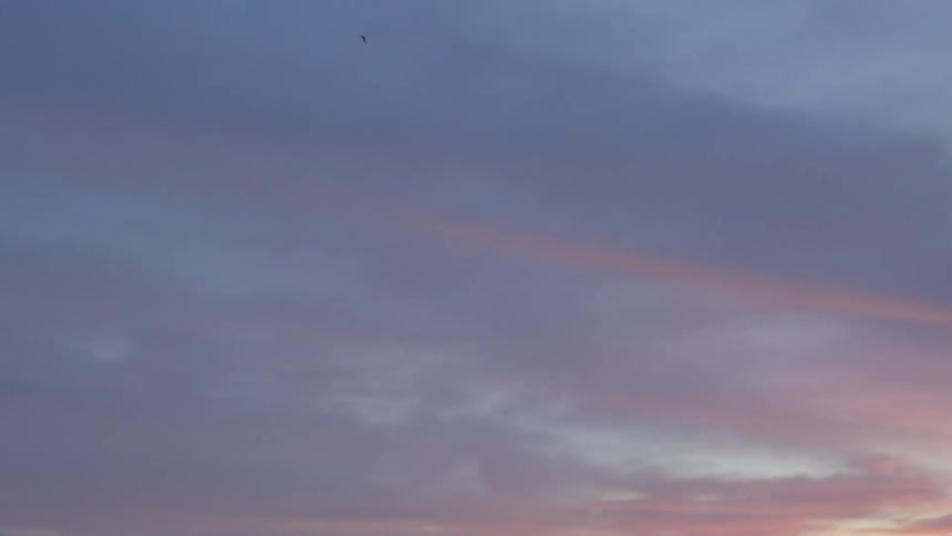 View of a large calm lake from its rocky shore on a cloudy day at dusk