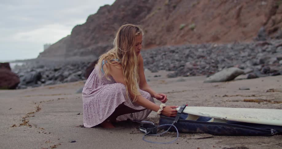 A woman is working on her surfboard at the beach