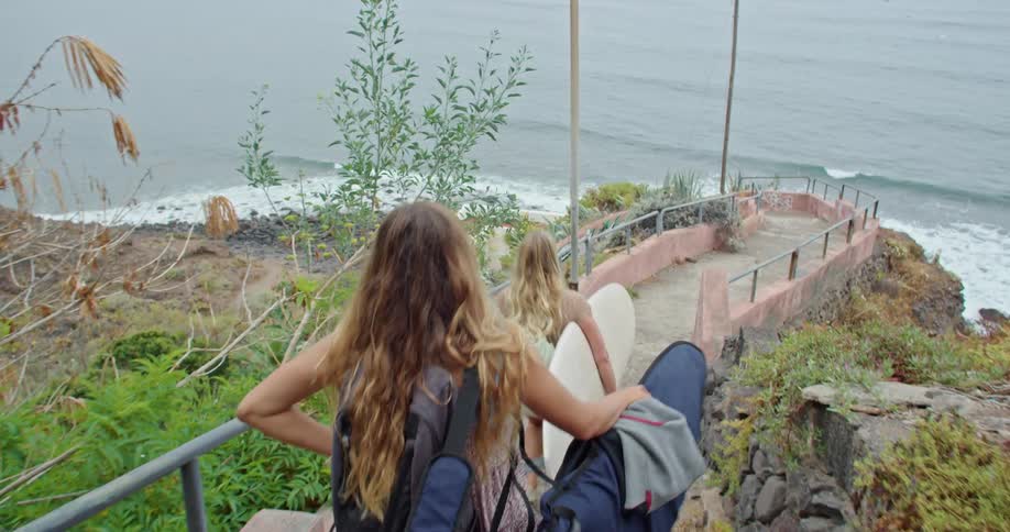 Two women walking down steps carrying surfboards