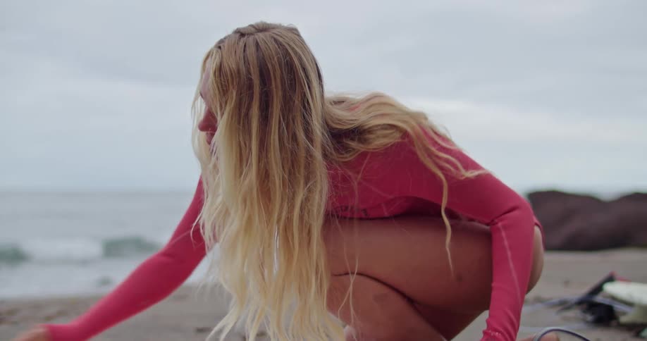 A woman on the beach is waxing her surfboard