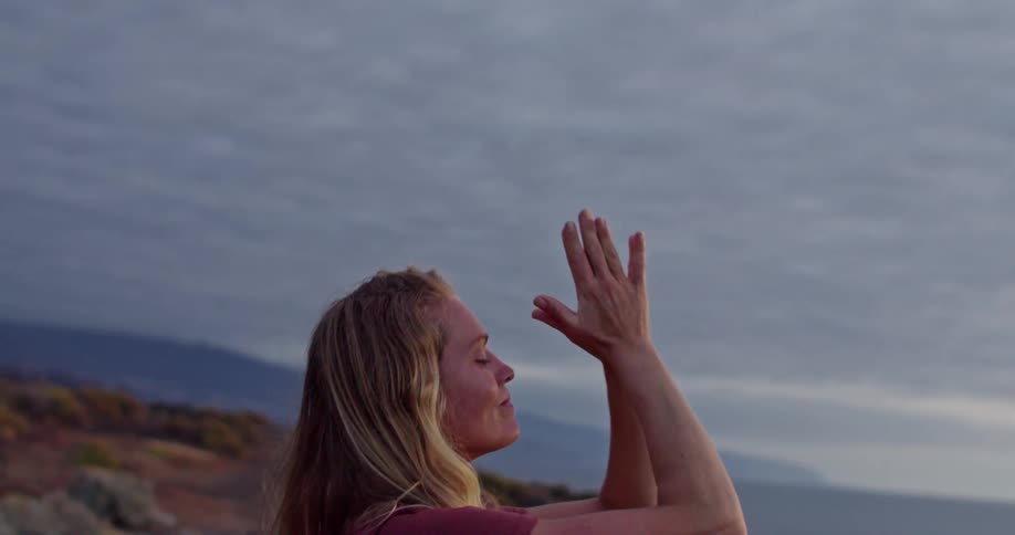 Blonde woman practices yoga on the cliff at sunrise
