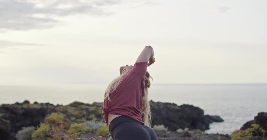 A woman stretching near a coast with the ocean sky and clouds in the background