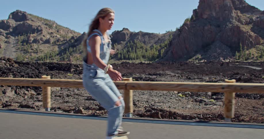 A woman is skateboarding down an empty road next to lava fields