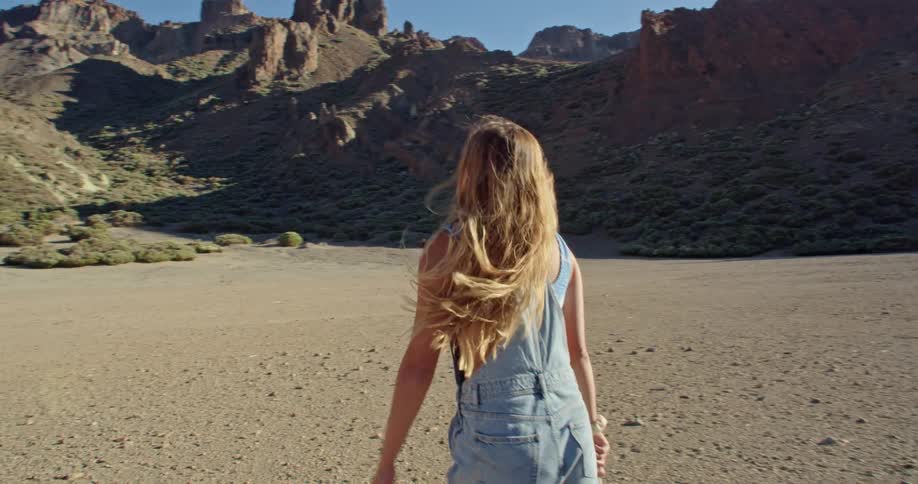 A woman is holding a stick and walking near mountains on sunny day