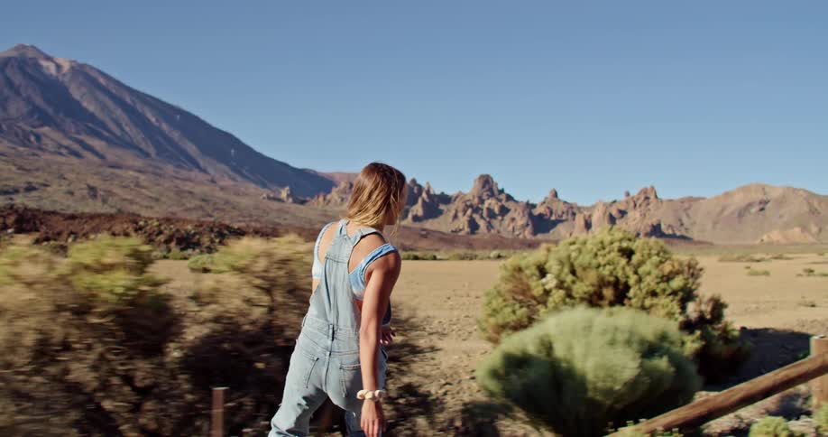 A woman on a skateboard with a mountain range the sky and clouds in the background