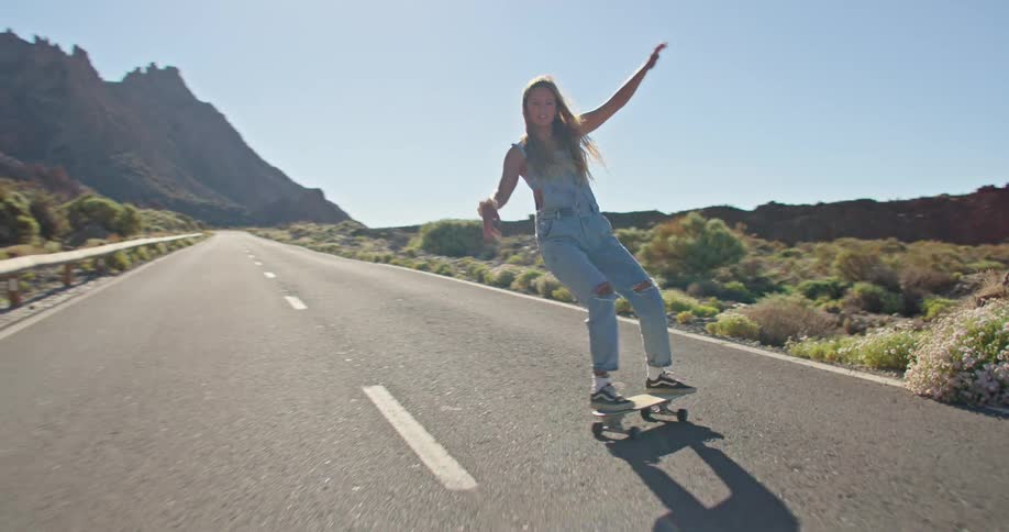A woman rides a skateboard down the middle of a narrow road near a canyon
