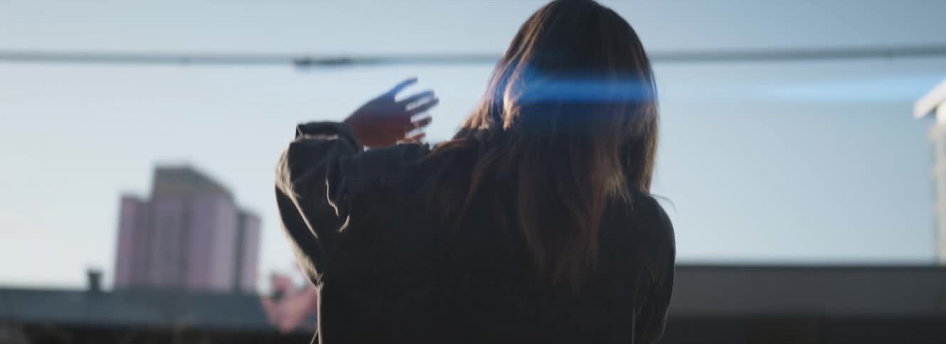 A woman is standing outside in a city holding her hand up to block the sun
