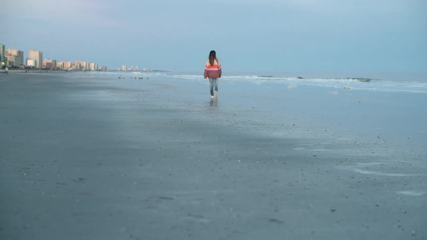 A female is walking along a beach near a city