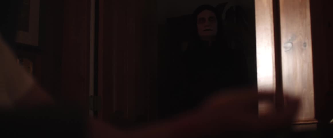 A person sits on the floor in front of a doorway in a dark room