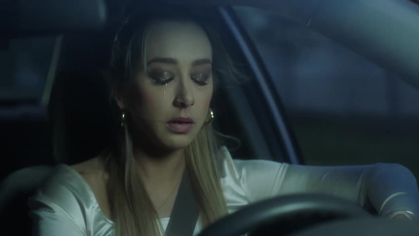 A woman cries and struggles to keep her eyes open while driving
