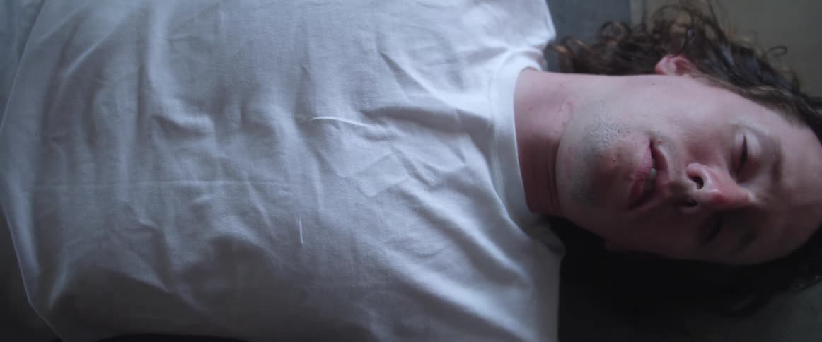 Young long haired man wearing white tshirt laying on the floor