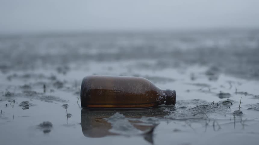 Empty bottle in muddy field while drizzling