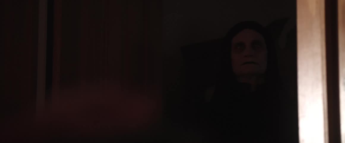 A person in a room hand with a woman a doorway and a wall in the background