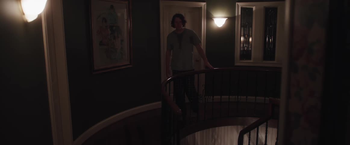A man in a room next to a banister with a wall a door and window in the background