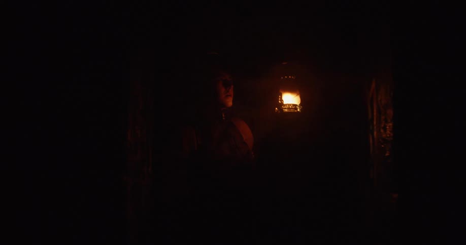 Woman carrying an antique gas lamp inside a dark cavern