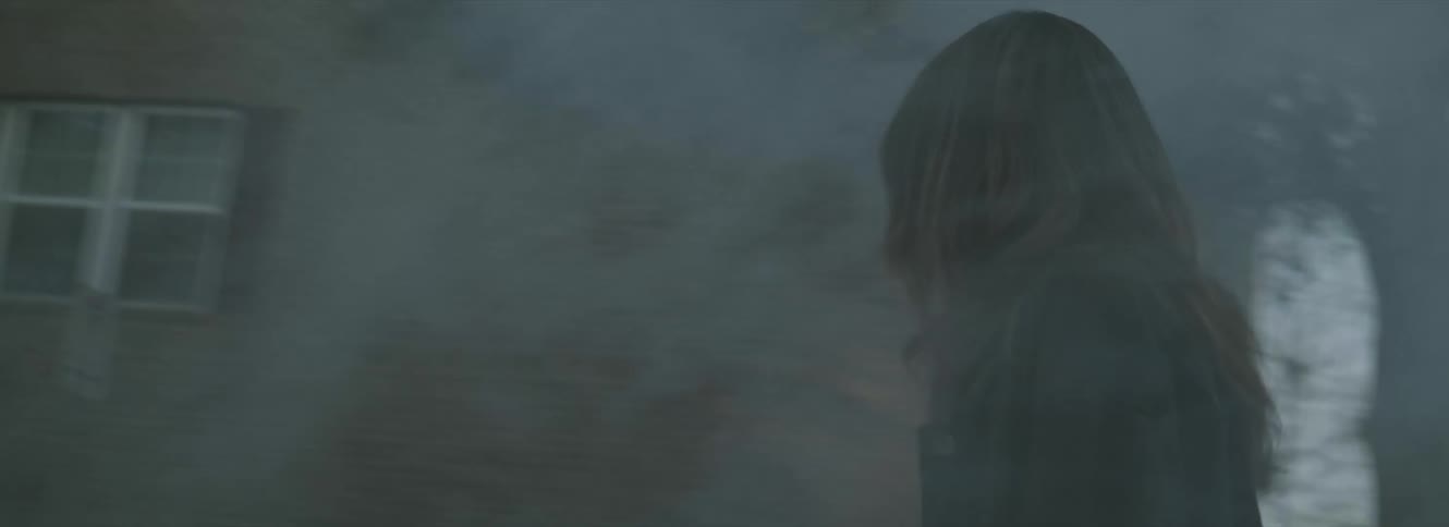 Woman with brown wavy hair dark denim jacket walks through smoke and looks around anxiously in the city street