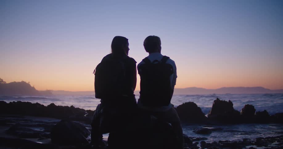 Silhouette of two people sitting on a rock at a beach as the waves roll in