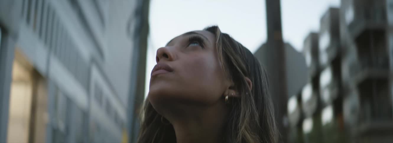A woman looks up at the sky near tall buildings